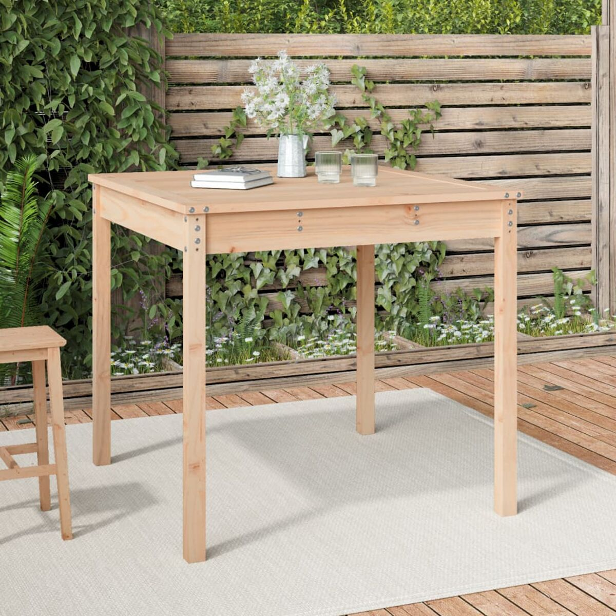 Holztisch und Stühle auf einem Deck. Blumen und ein Buch auf dem Tisch. Holzzaun im Hintergrund.