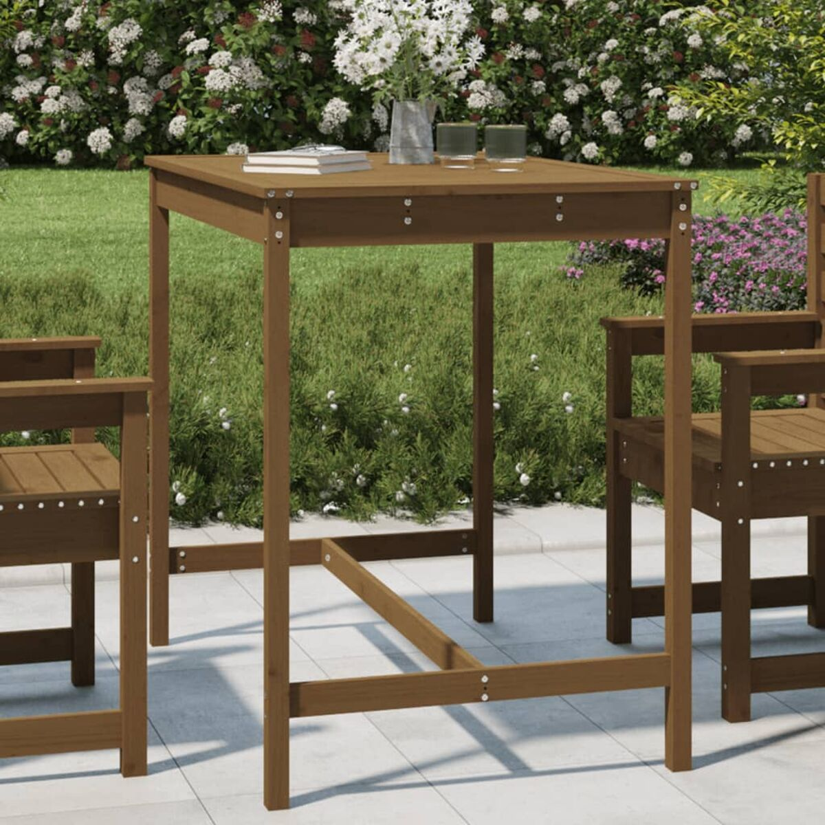 Holztisch und Stühle auf der Terrasse, mit Blumen in einer Vase. Grüne Pflanzen im Hintergrund.