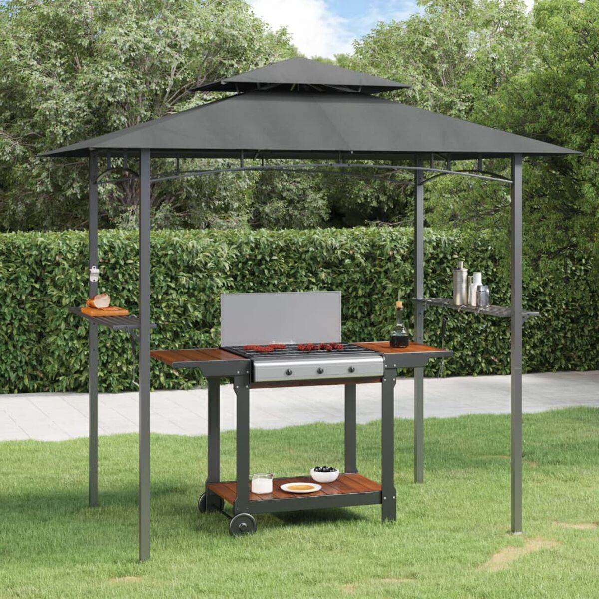 Ein grauer Pavillon mit Grill, Beistelltischen und einem unteren Regal steht in einem Rasen mit einer Hecke.