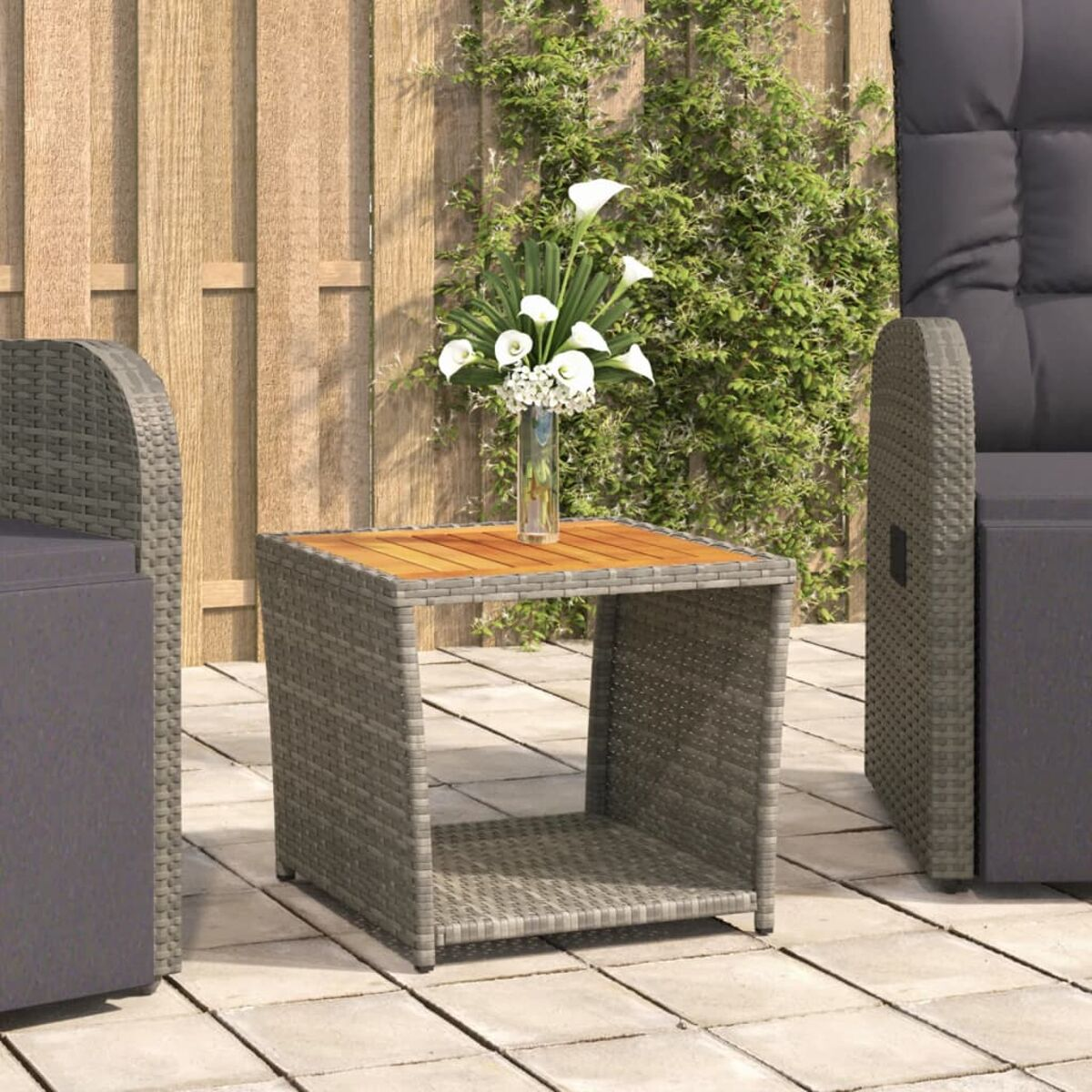 Ein grauer Webetisch mit Holzplatte. Blumen in einer Vase. Graue Stühle auf einer Terrasse.