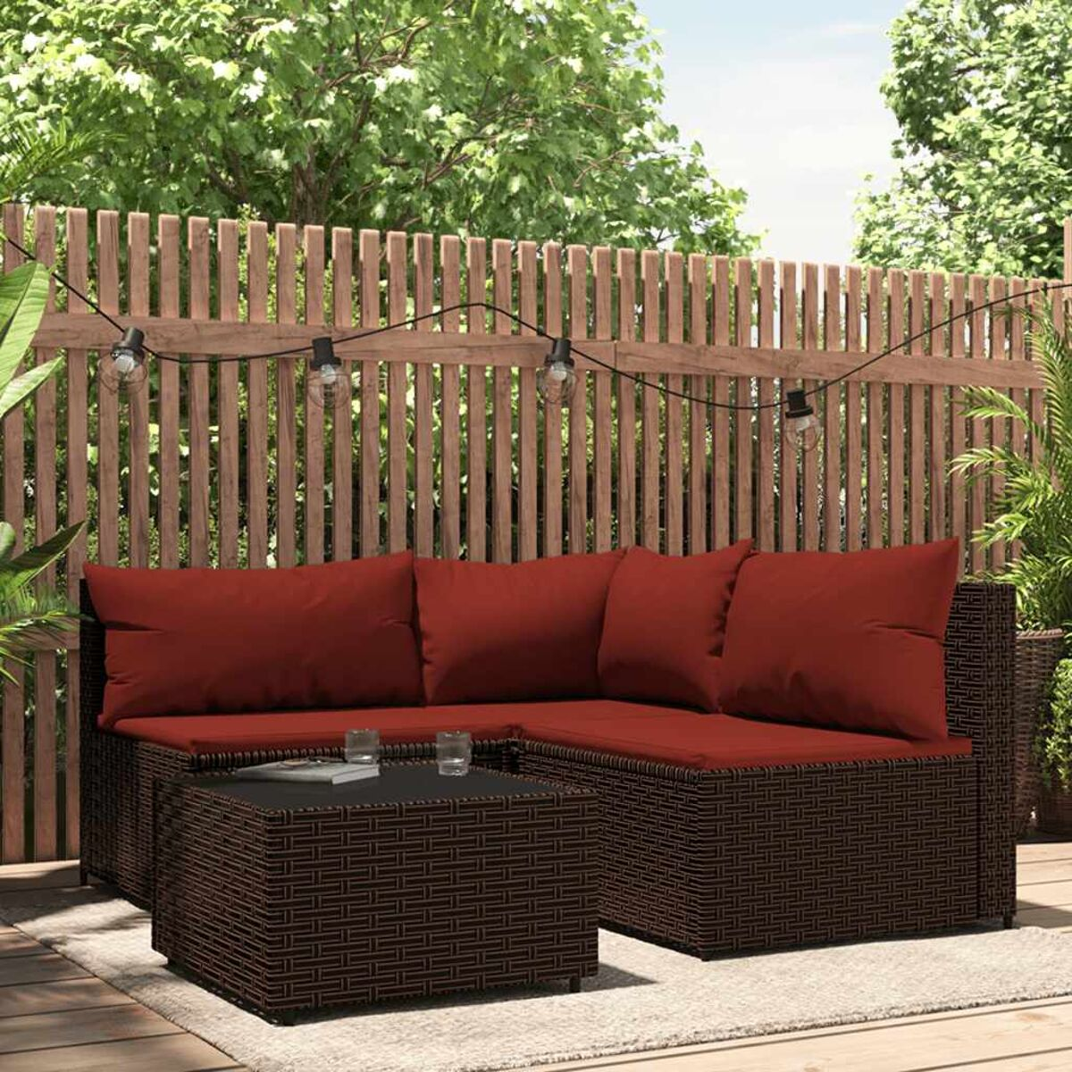 Outdoor-Rattansofa-Set mit roten Kissen vor Holzzaun.