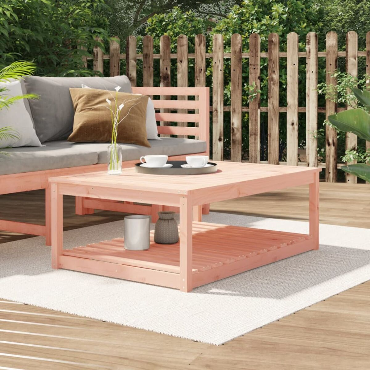 Rosa Holztisch im Freien mit Gegenständen darauf, auf einem Teppich. Holzsofa dahinter.