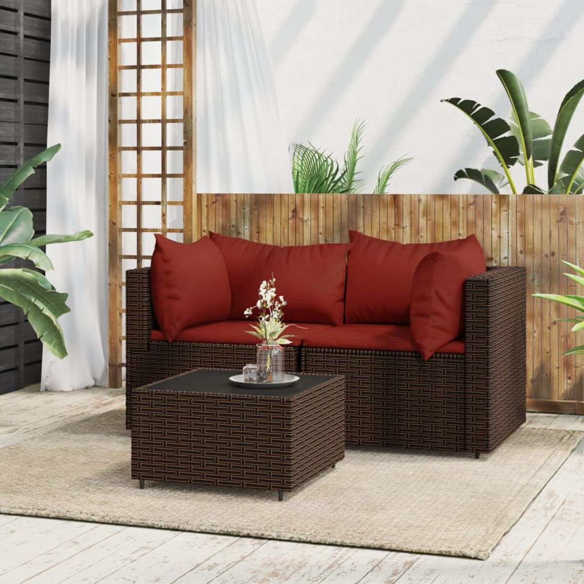 Outdoor-Rattan-Sofagarnitur mit roten Kissen und einem kleinen Tisch, auf einem Teppich.