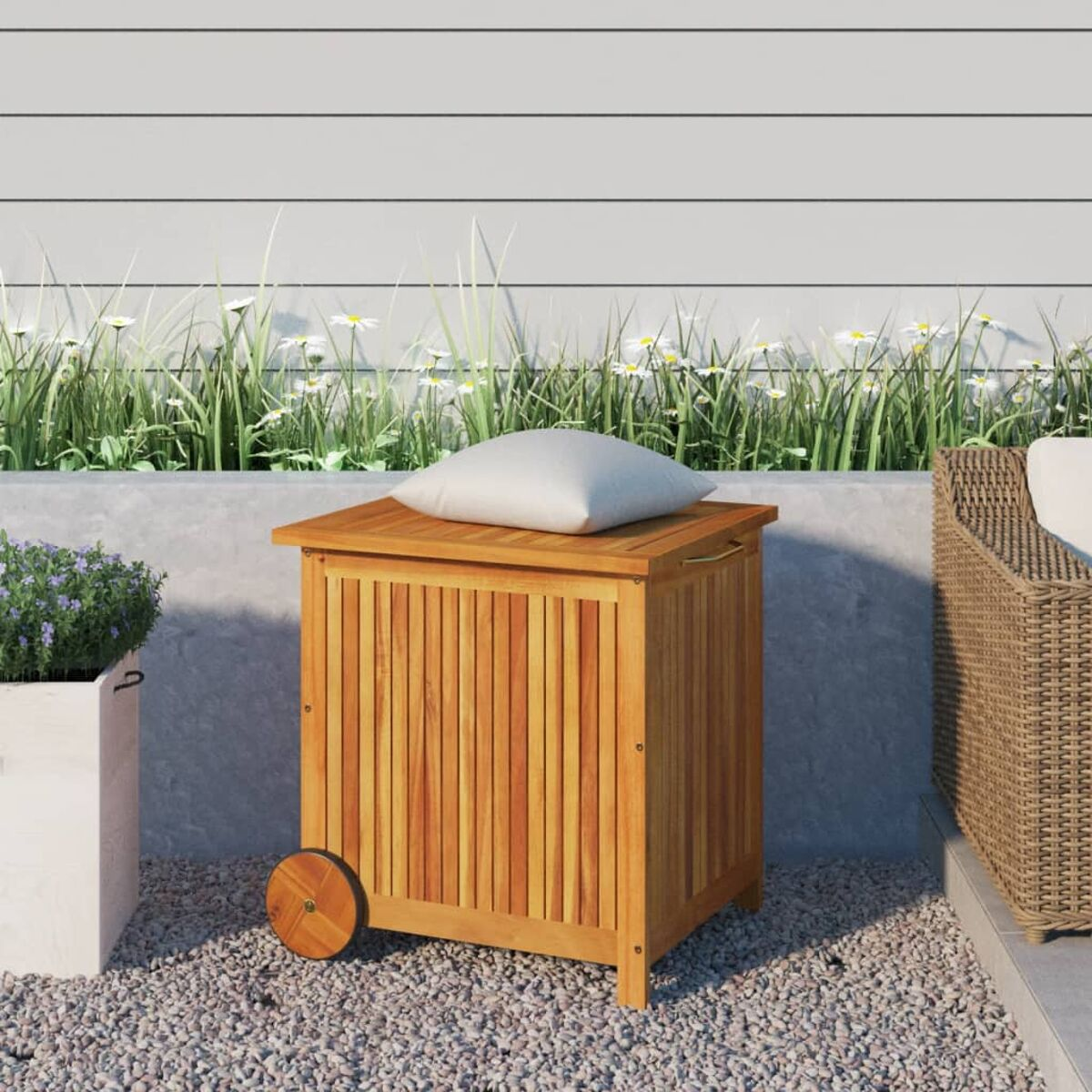Holzbox mit Kissen auf Kies. Gänseblümchen und Grün im Hintergrund.