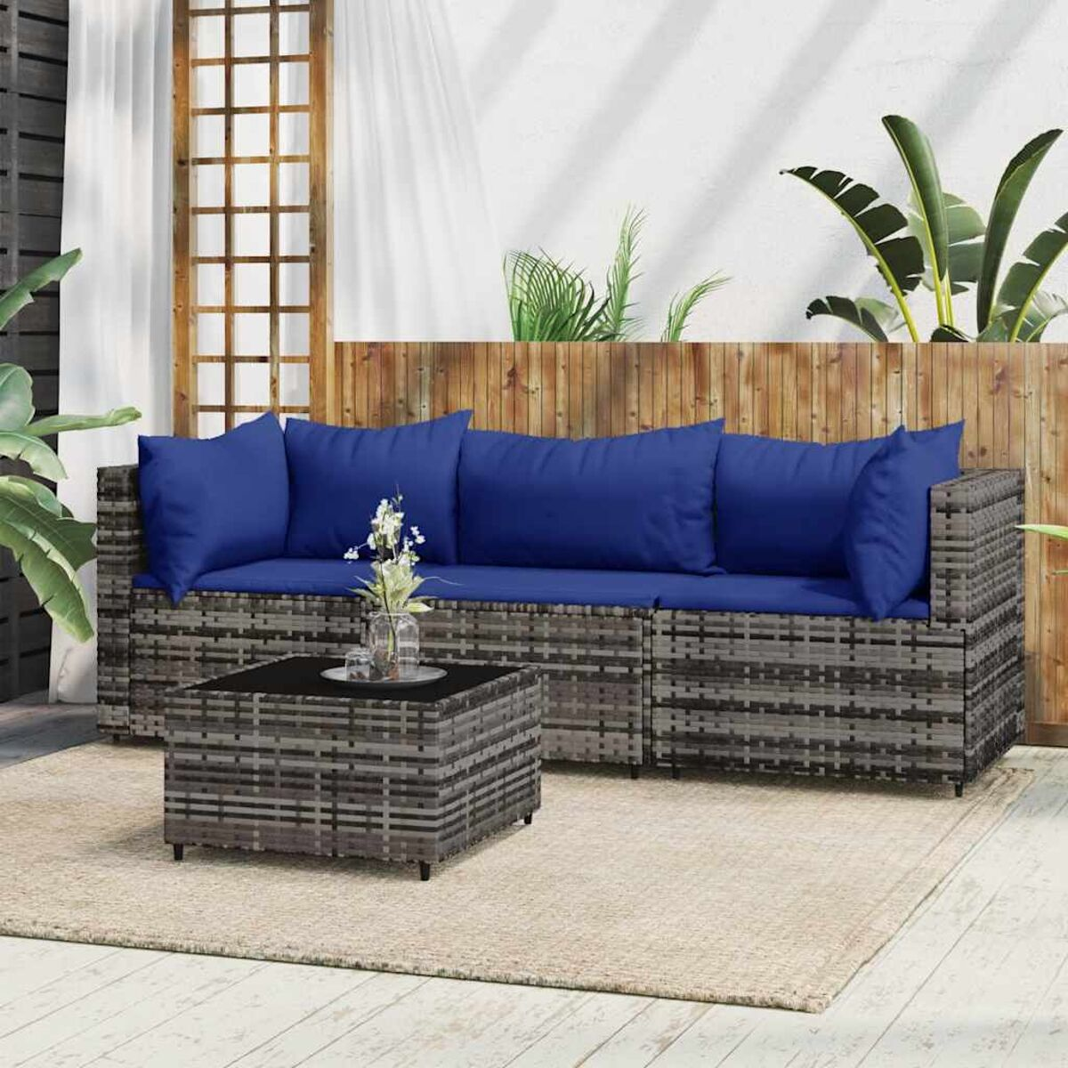 Rattansofa mit blauen Kissen, einem Couchtisch und Pflanzen im Hintergrund.