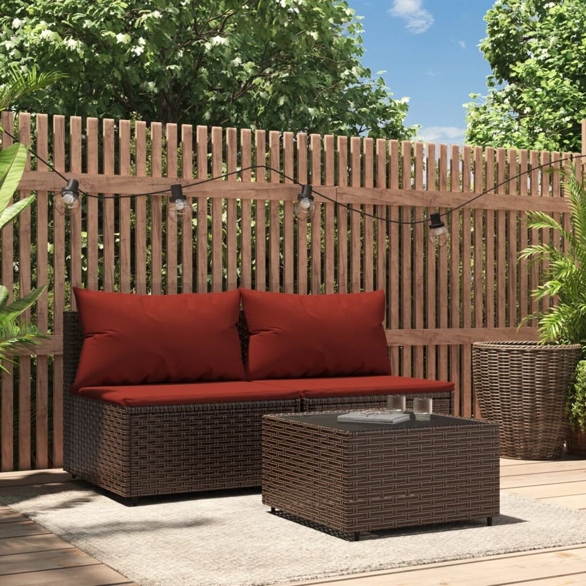 Braunes Outdoor-Set aus Korbgeflecht mit roten Kissen. Enthält ein Sofa und einen Tisch. Lichterketten hängen.