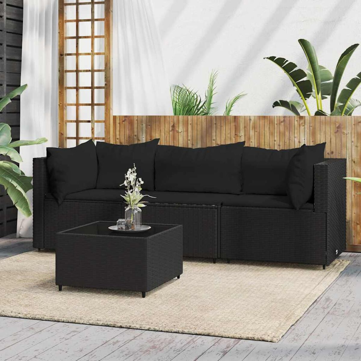Schwarzes Rattan-Outdoor-Sofa mit Kissen und einem Couchtisch mit Glasplatte auf einem beigefarbenen Teppich.