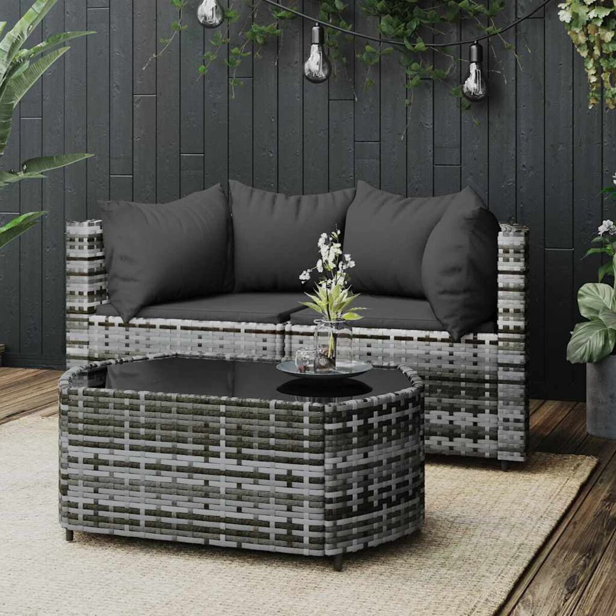 Outdoor-Sitzgruppe: Sofa und Tisch. Gewebte graue Möbel. Pflanzen und Lichter im Hintergrund.