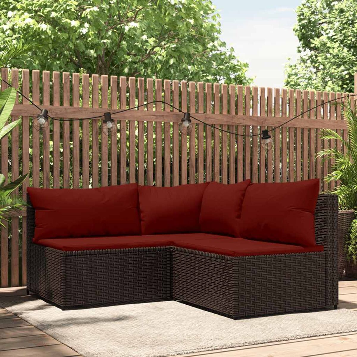 Ein dunkelbraunes Rattan-Ecksofa mit roten Kissen. Ein Holzzaun im Hintergrund.