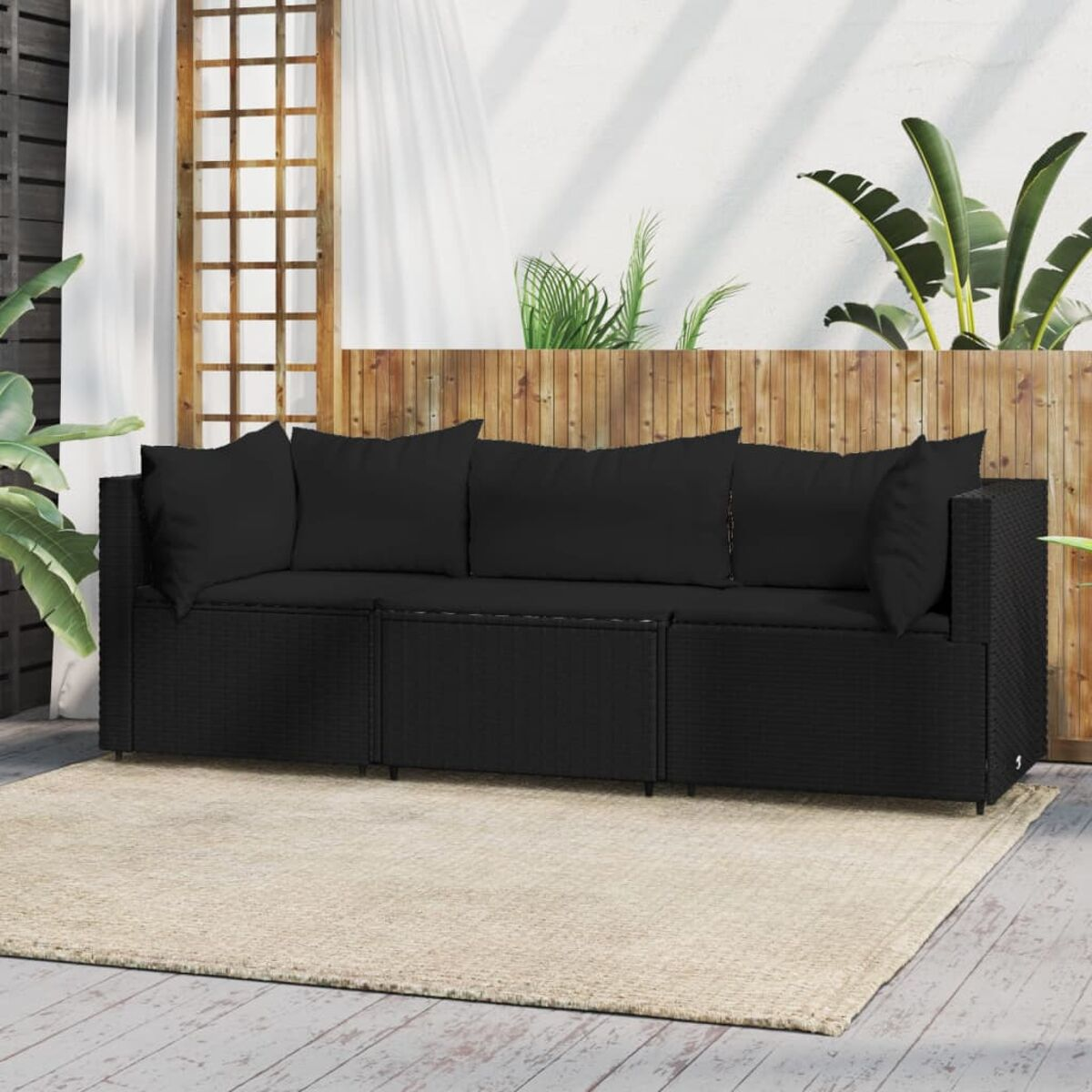 Schwarzes Outdoor-Sofaset aus Korbgeflecht mit Kissen, auf einem beigen Teppich auf einer Terrasse.