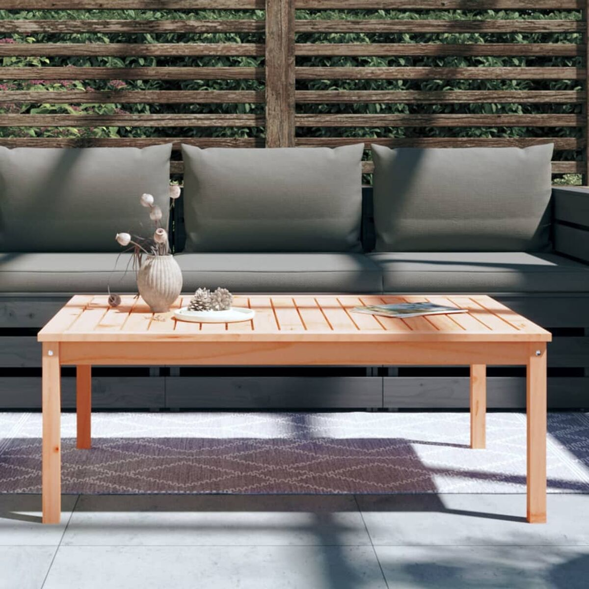 Holztisch mit Vase, Blumen, und Deko, mit Sofa und Kissen im Hintergrund.