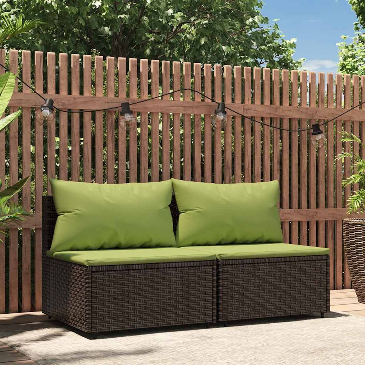 Braunes Outdoor-Sofa aus Korbgeflecht mit grünen Kissen. Ein Holzzaun im Hintergrund.