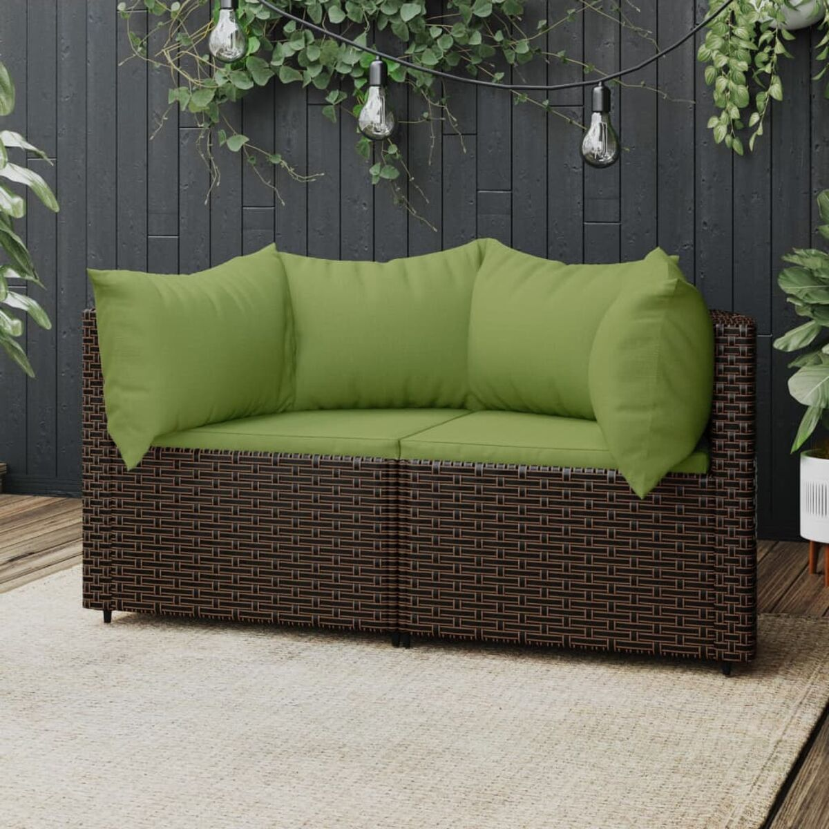 Ein braunes Korbssofa mit grünen Kissen. Das Sofa steht auf einem Teppich mit Lichterketten darüber.
