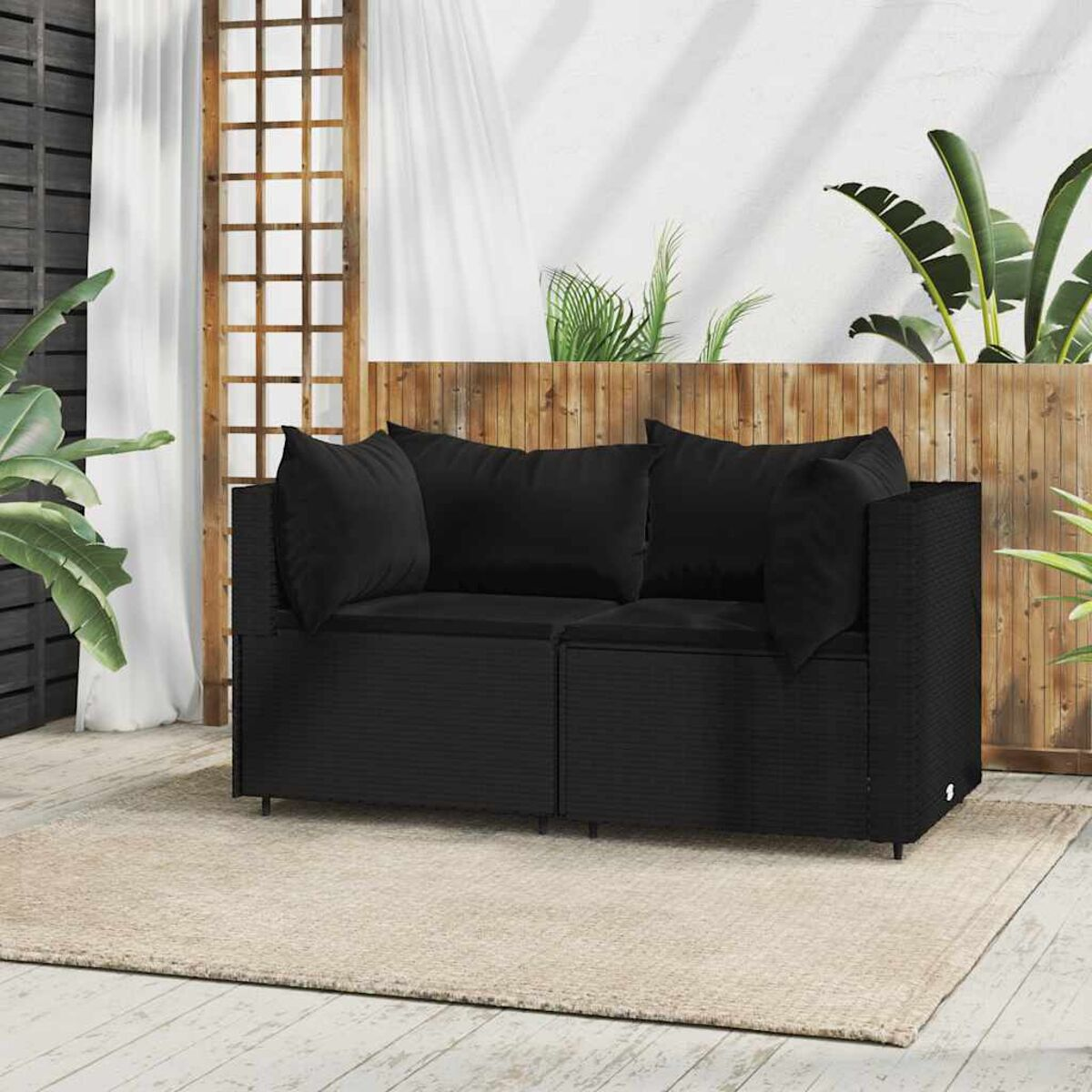 Schwarzes Rattansofa-Set mit Kissen auf beigem Teppich.