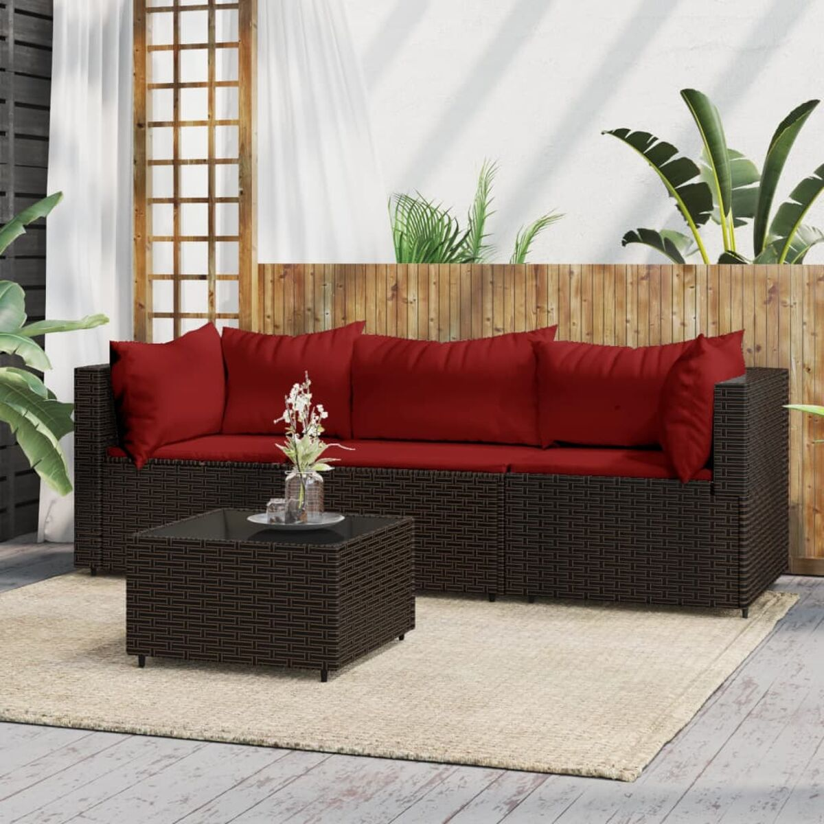 Dunkelbraunes Korbmöbel-Sofa mit roten Kissen und passendem Couchtisch. Hintergrund: Holzzaun.