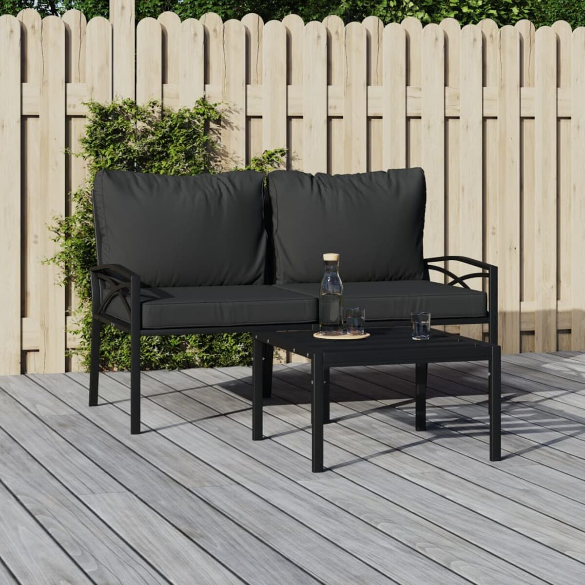 Ein schwarzes Metallsofa und Tisch-Set auf einem Holzdeck. Zwei Stühle und eine Flasche auf dem Tisch.
