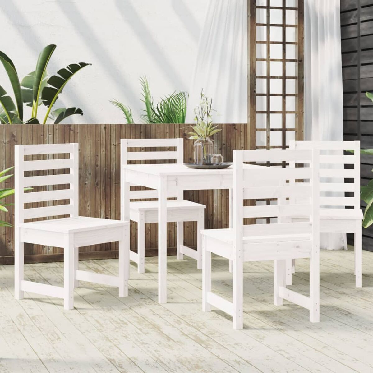 Weißes Holz-Ess-Set im Freien: Tisch, Stühle und Hintergrund aus Pflanzen und Holzpaneelen auf einem Holzdeck.