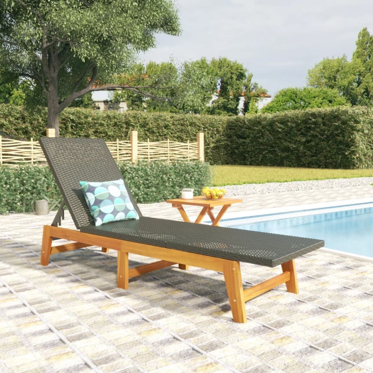 Liegestuhl am Pool, kleiner Tisch mit Obst. Grüne Bäume und eine Hecke im Hintergrund.