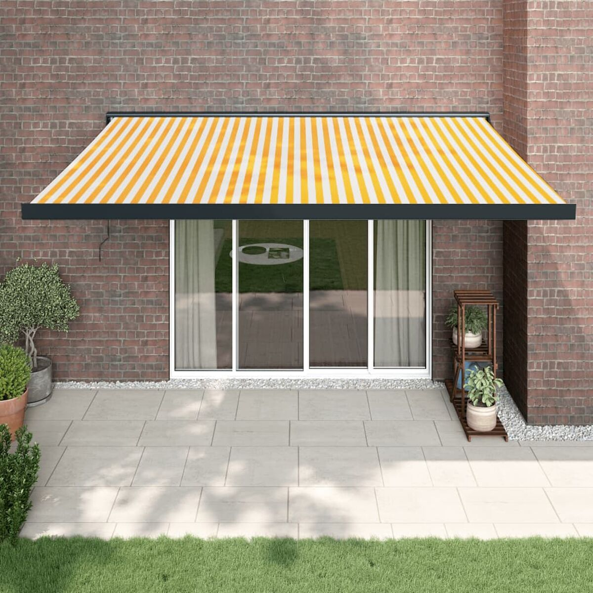 Haus mit gestreifter Markise, Backsteinmauer und Glastüren. Topfpflanzen auf der Terrasse.