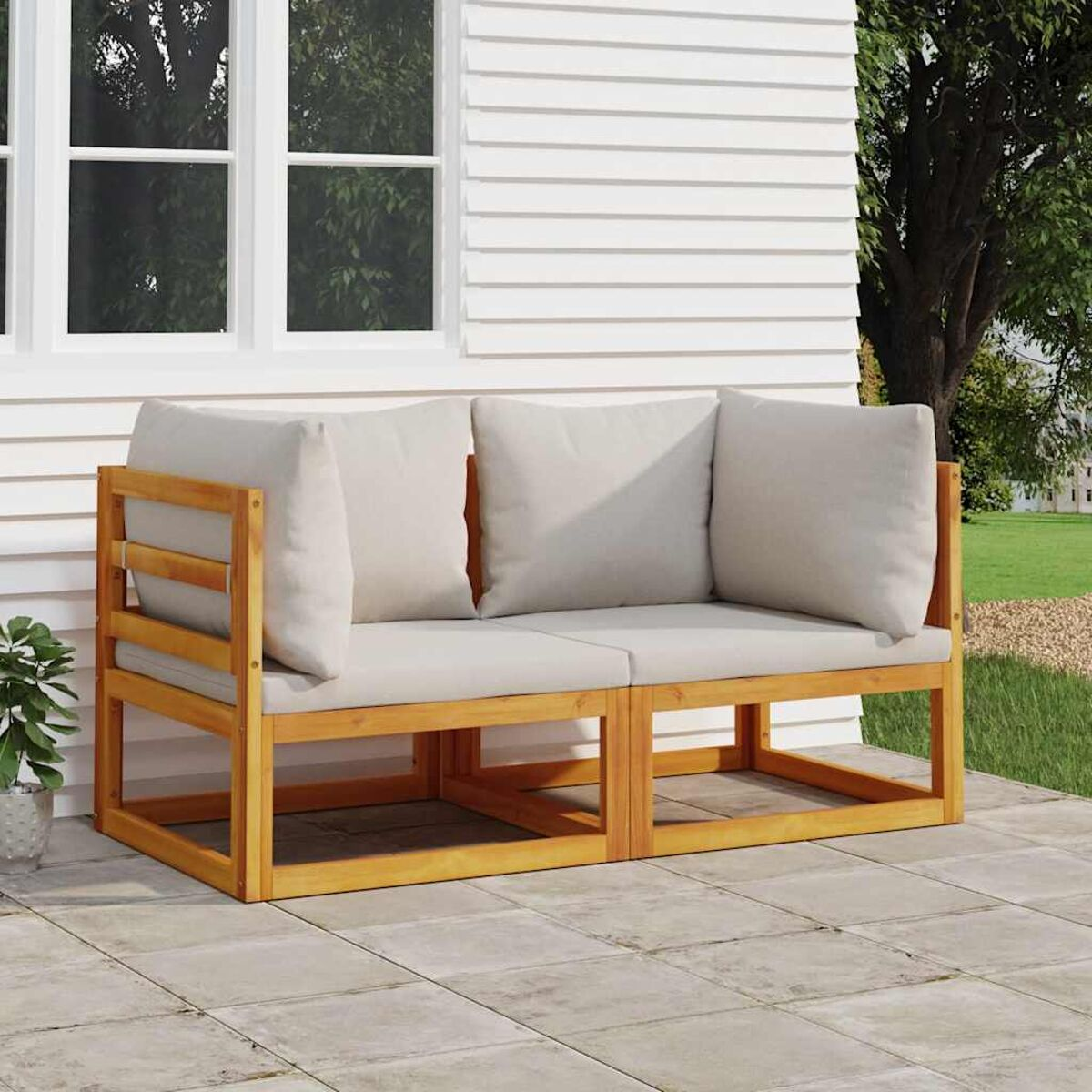 Outdoor-Sofa aus Holz mit zwei Kissen, auf einer Terrasse in der Nähe eines weißen Hauses.