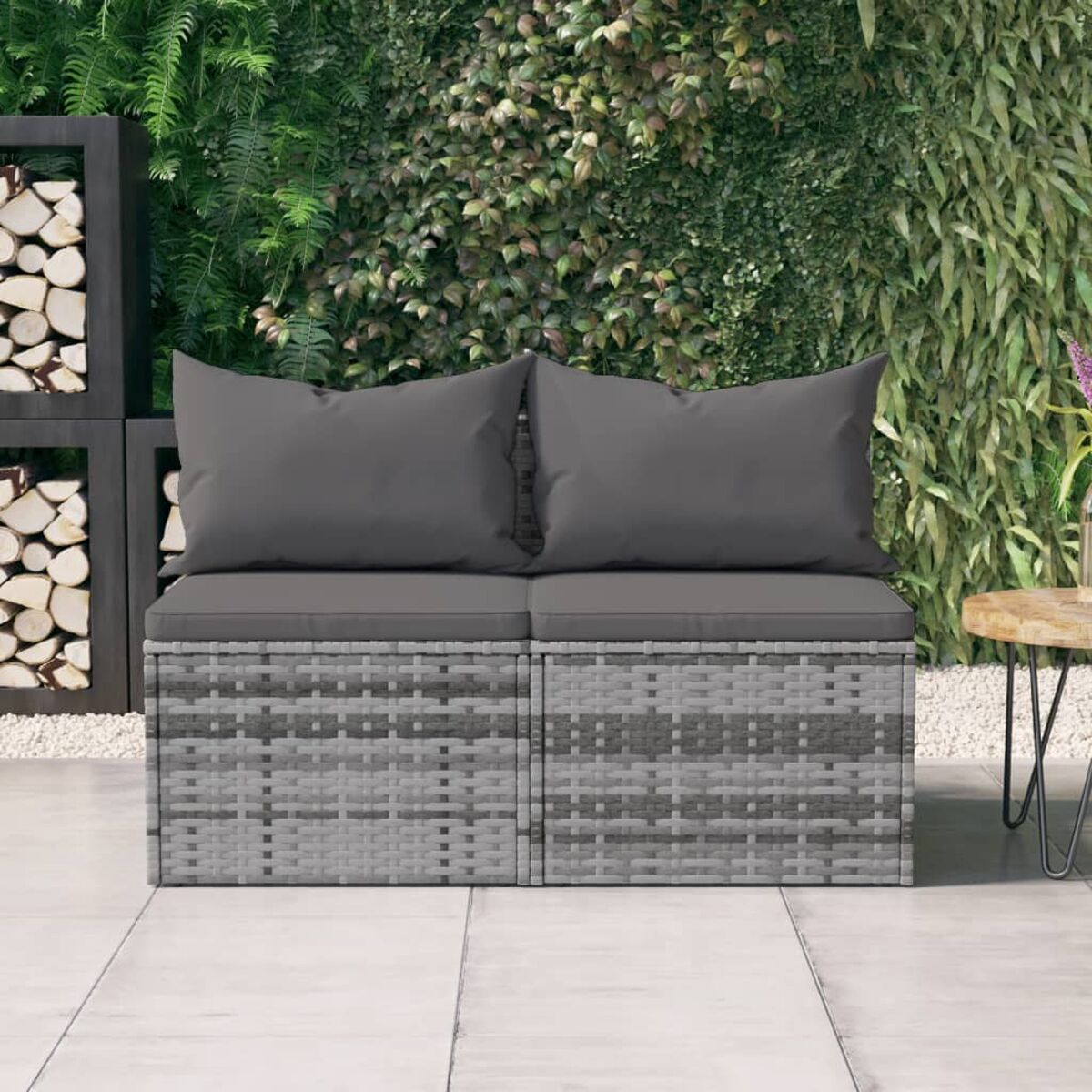 Ein graues Rattan-Zweisitzer-Sofa mit grauen Kissen. Das Sofa steht auf einer Terrasse.