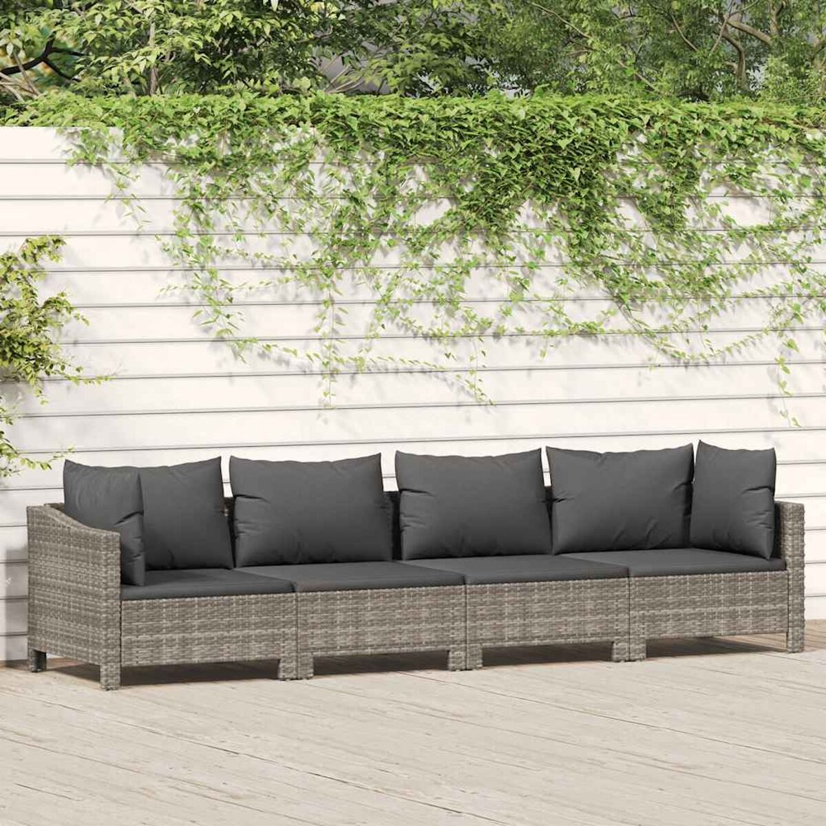 Ein graues Korbsessel-Sofa mit dunkelgrauen Kissen, vor einem weißen Zaun mit Kletterpflanzen.