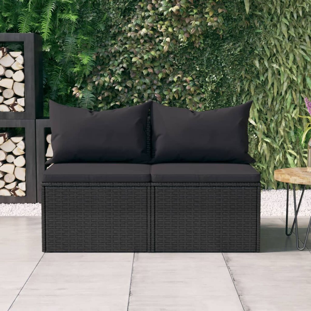 Schwarzes Outdoor-Sofa aus Korbgeflecht mit schwarzen Kissen. Auf einer Terrasse mit grünem Hintergrund.