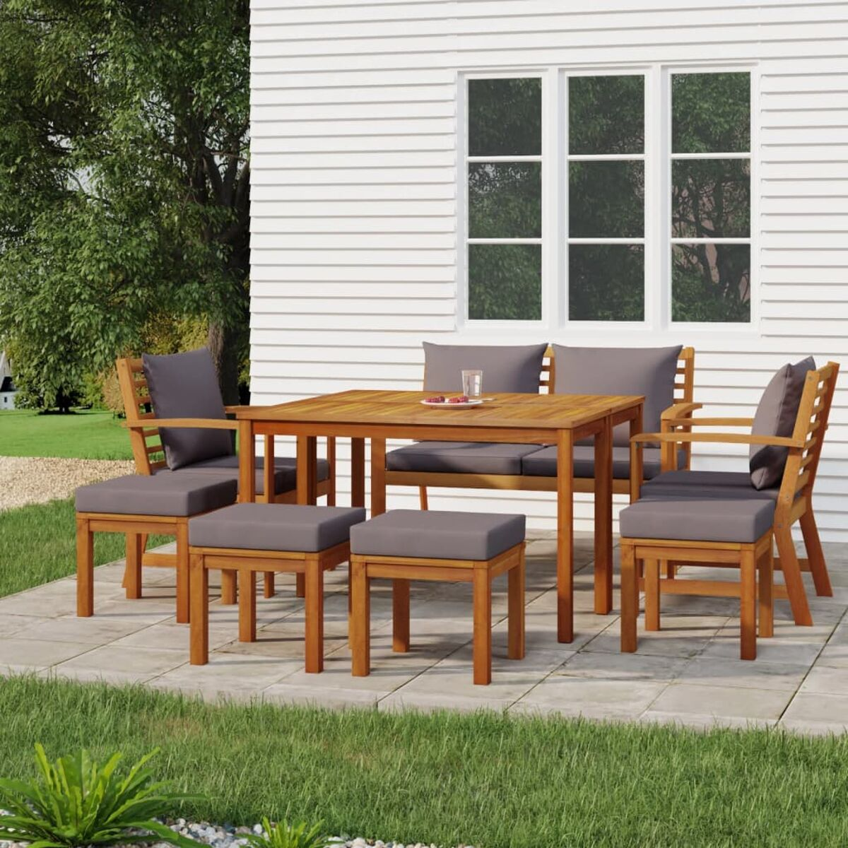 Gartenmöbel-Set auf einer Terrasse, mit Tisch, Stühlen und Hockern. Graue Kissen.