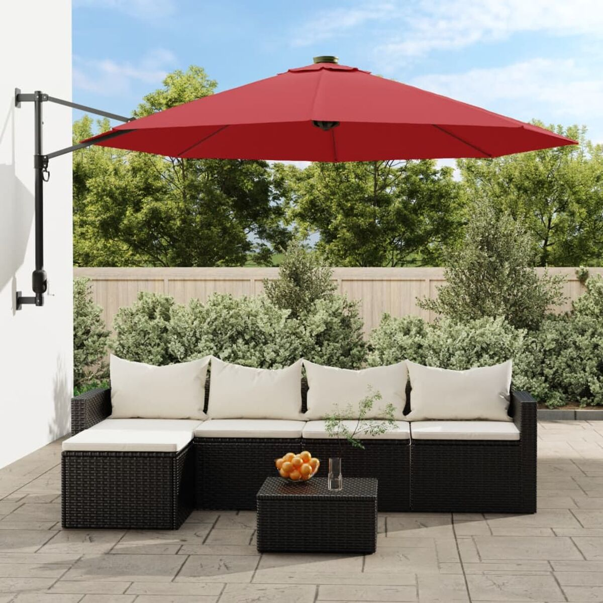 Schwarzes Korbmöbel-Set mit weißen Kissen, rotem Sonnenschirm und kleinem Tisch auf einer Terrasse.
