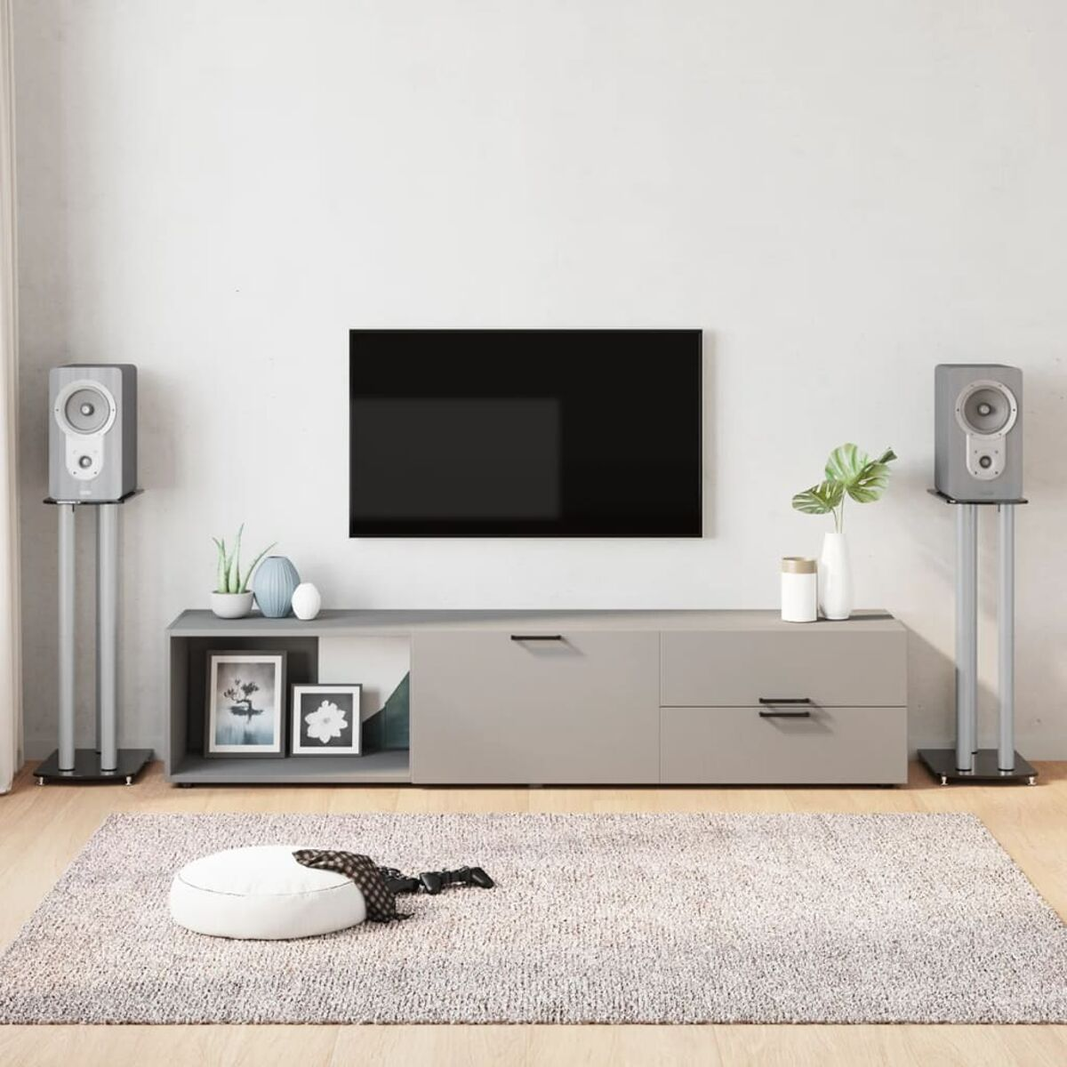 Wohnzimmer mit TV, Lautsprechern und Deko auf grauem Teppich.