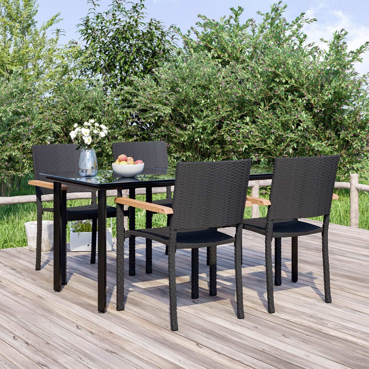 Schwarzer Tisch und Stühle. Schwarze gewebte Stühle mit Holzarmlehnen. Holzdeck, grüner Hintergrund.