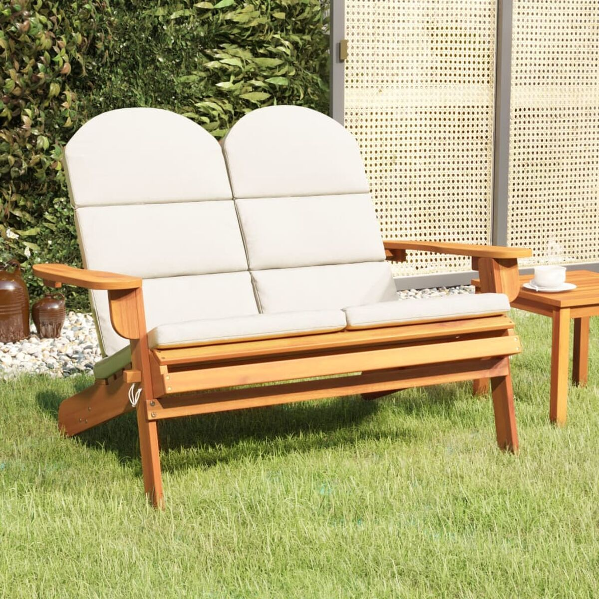 Holz-Lovesitz im Freien mit beigen Kissen, auf grünem Gras, mit einem kleinen Tisch.