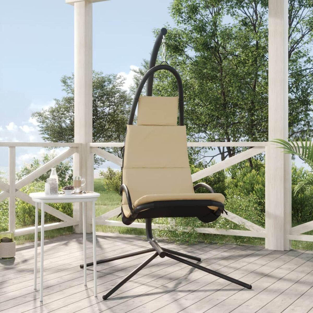 Beiger Hängestuhl auf einer Veranda mit weißem Tisch, Getränken und Bäumen im Hintergrund.