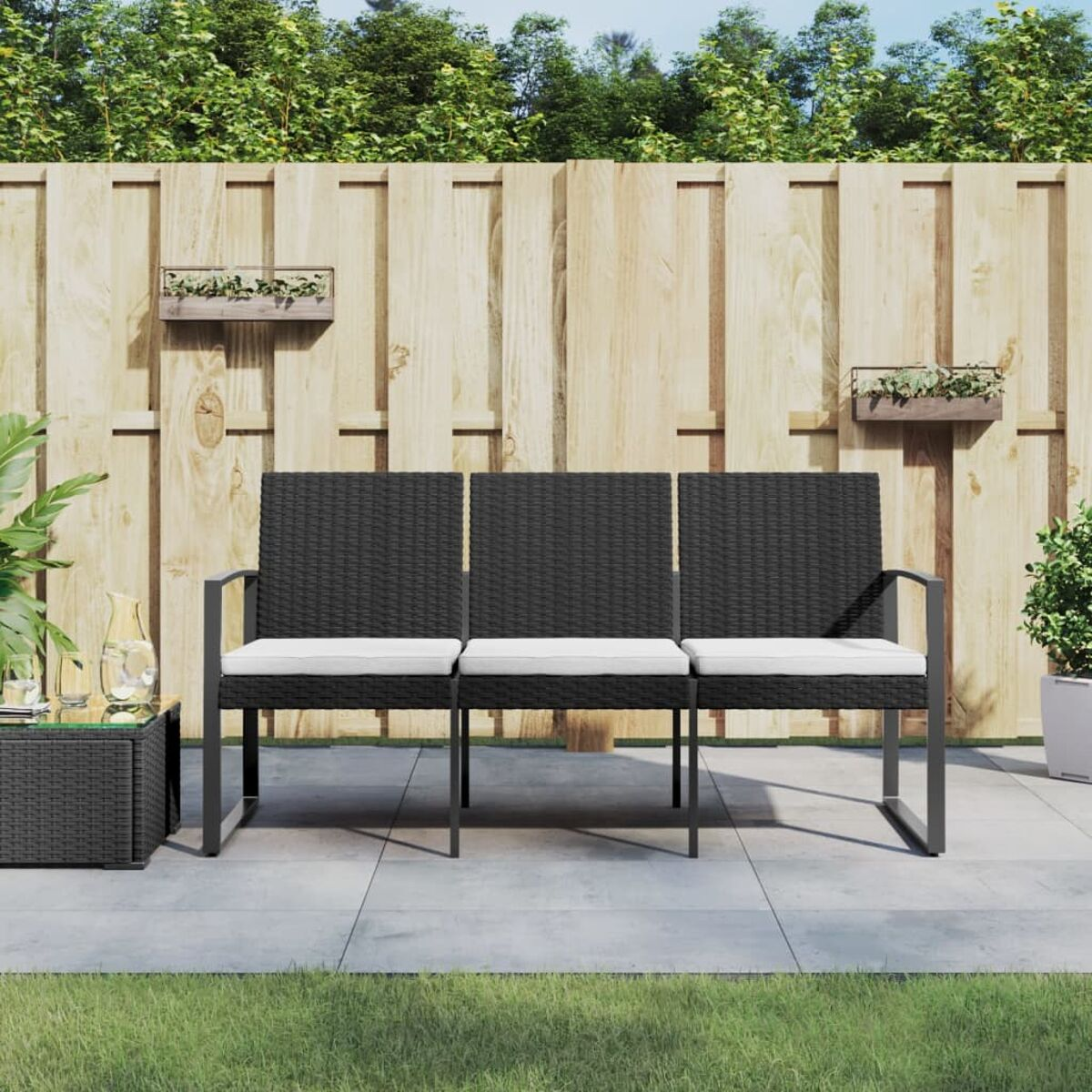 Schwarzes Outdoor-Sofa mit weißen Kissen. Es steht auf einer Terrasse mit Holzzaun und Pflanzen.