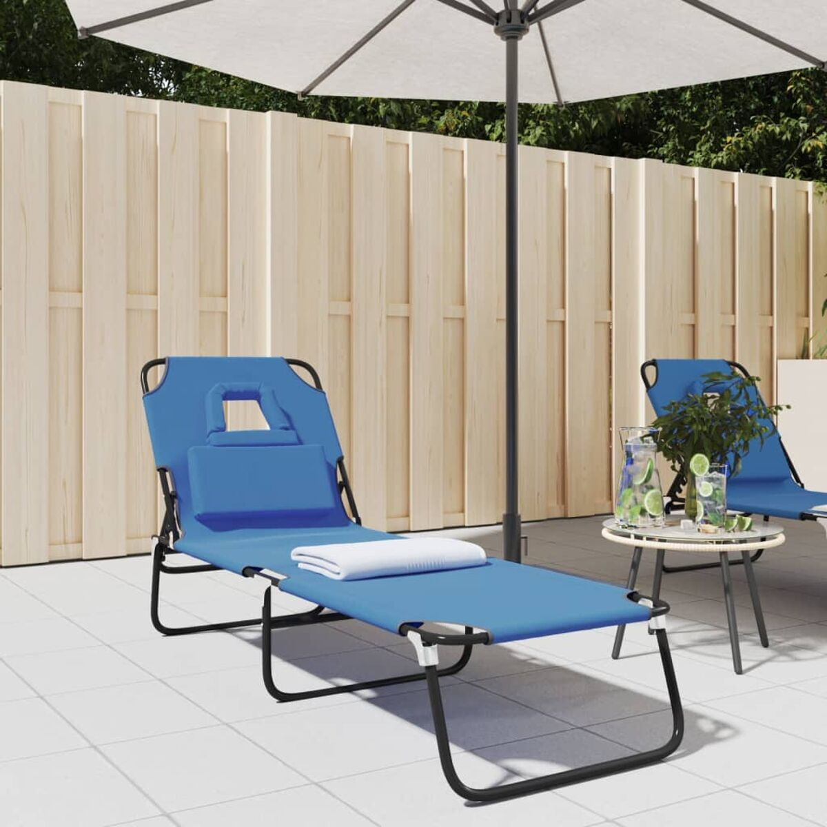 Blauer Liegestuhl mit weißem Handtuch, weißem Schirm und Beistelltisch auf Terrasse.