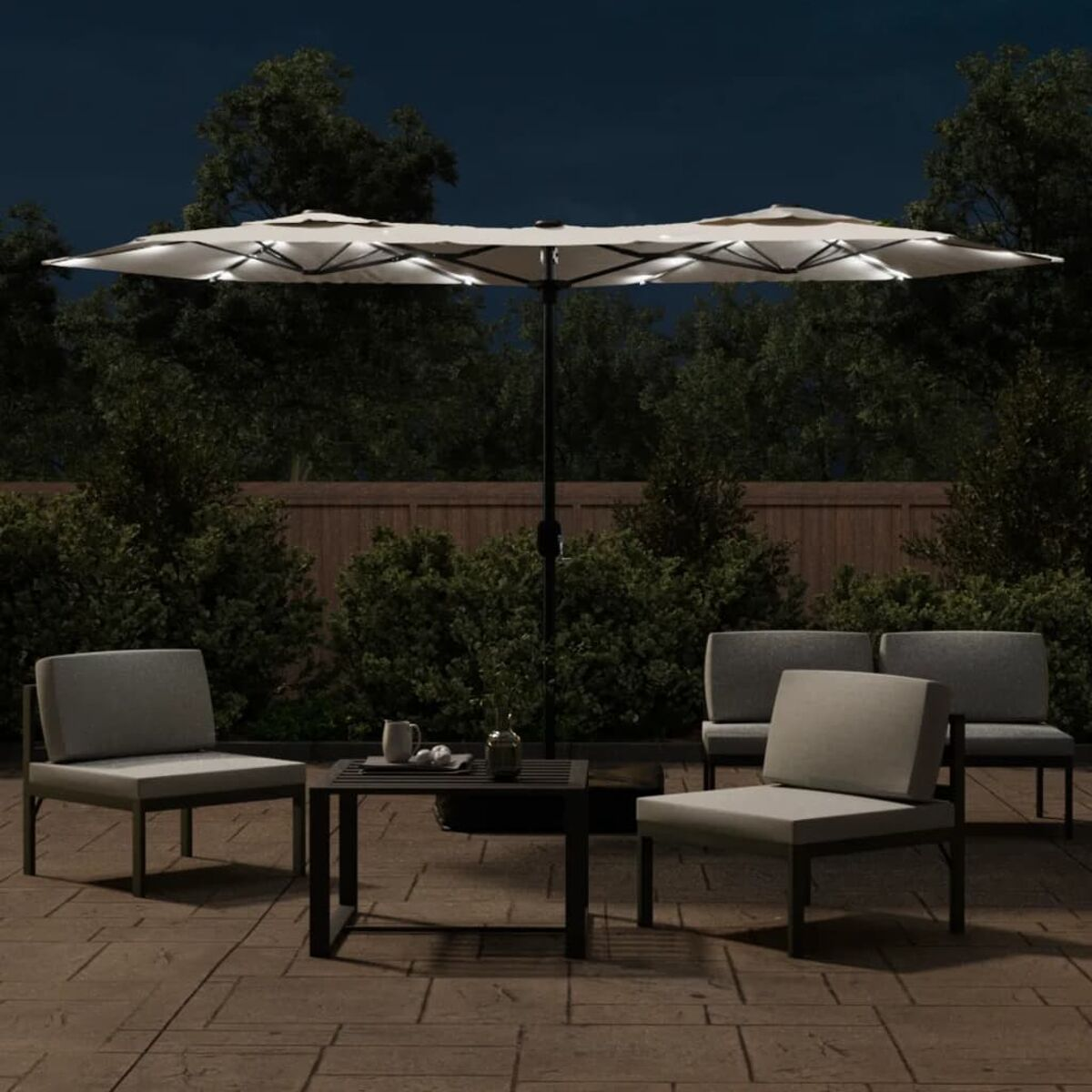 Sitzbereich im Freien bei Nacht. Beleuchteter Regenschirm, Stühle und Tisch. Dunkler Hintergrund mit Bäumen und Himmel. Gemütliche Atmosphäre.