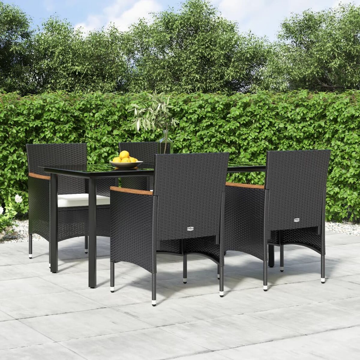 Ein Terrassenset mit einem schwarzen Glastisch und vier schwarzen Korbstühlen. Grüne Hecke im Hintergrund.