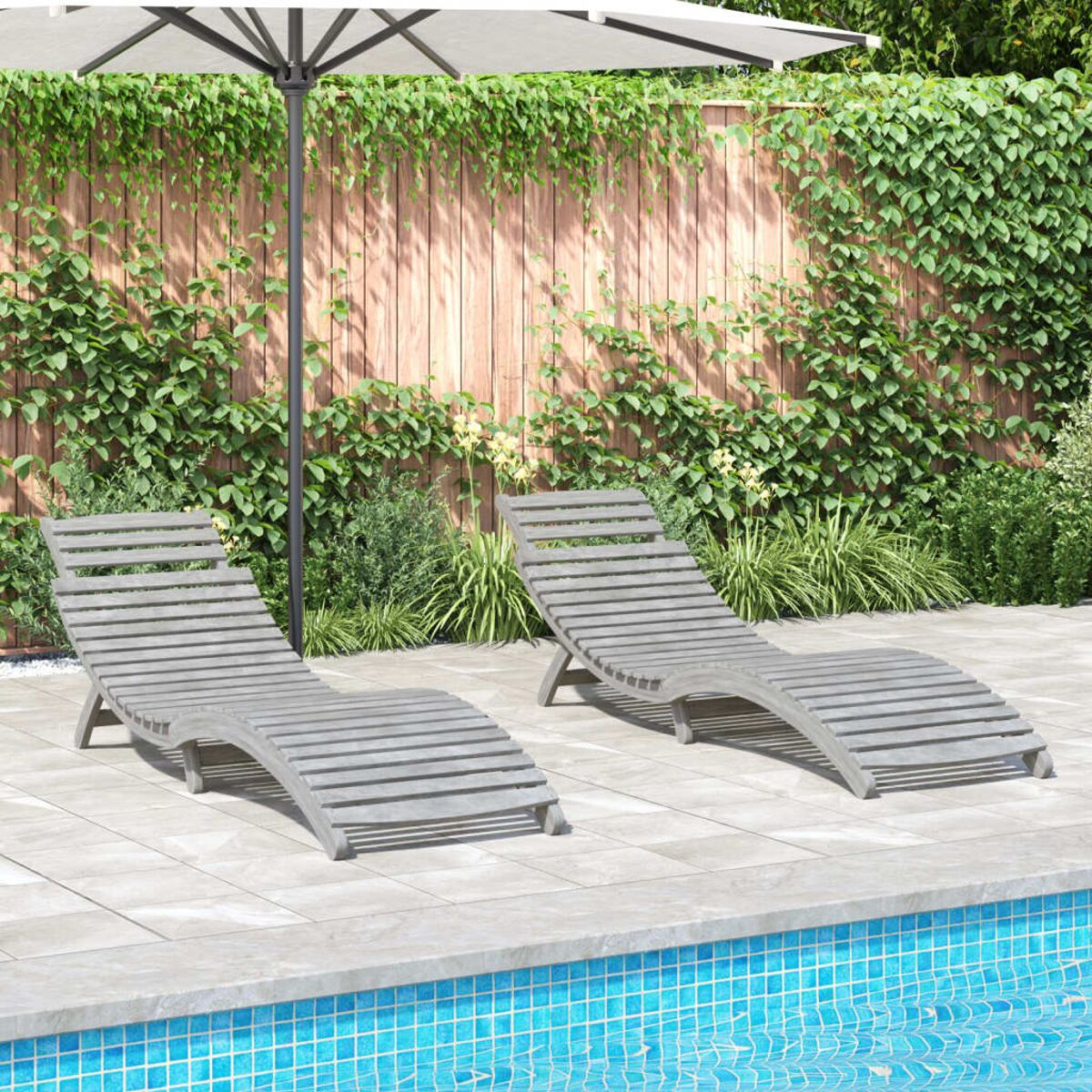 Zwei graue Liegestühle an einem Pool. Grüne Pflanzen und Holzzaun im Hintergrund.