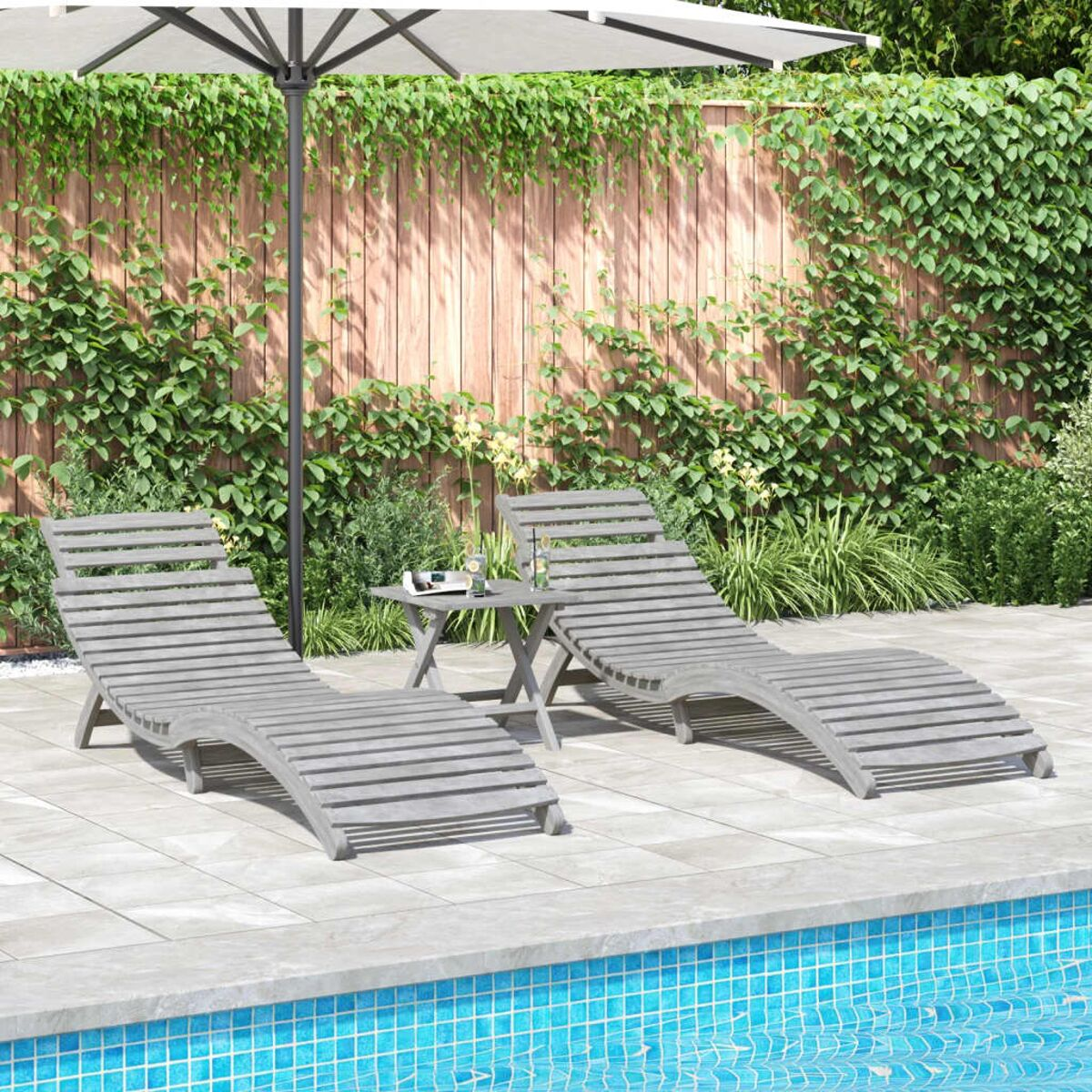 Zwei graue Sonnenliegen und kleiner Tisch am Pool. Gartenhintergrund.