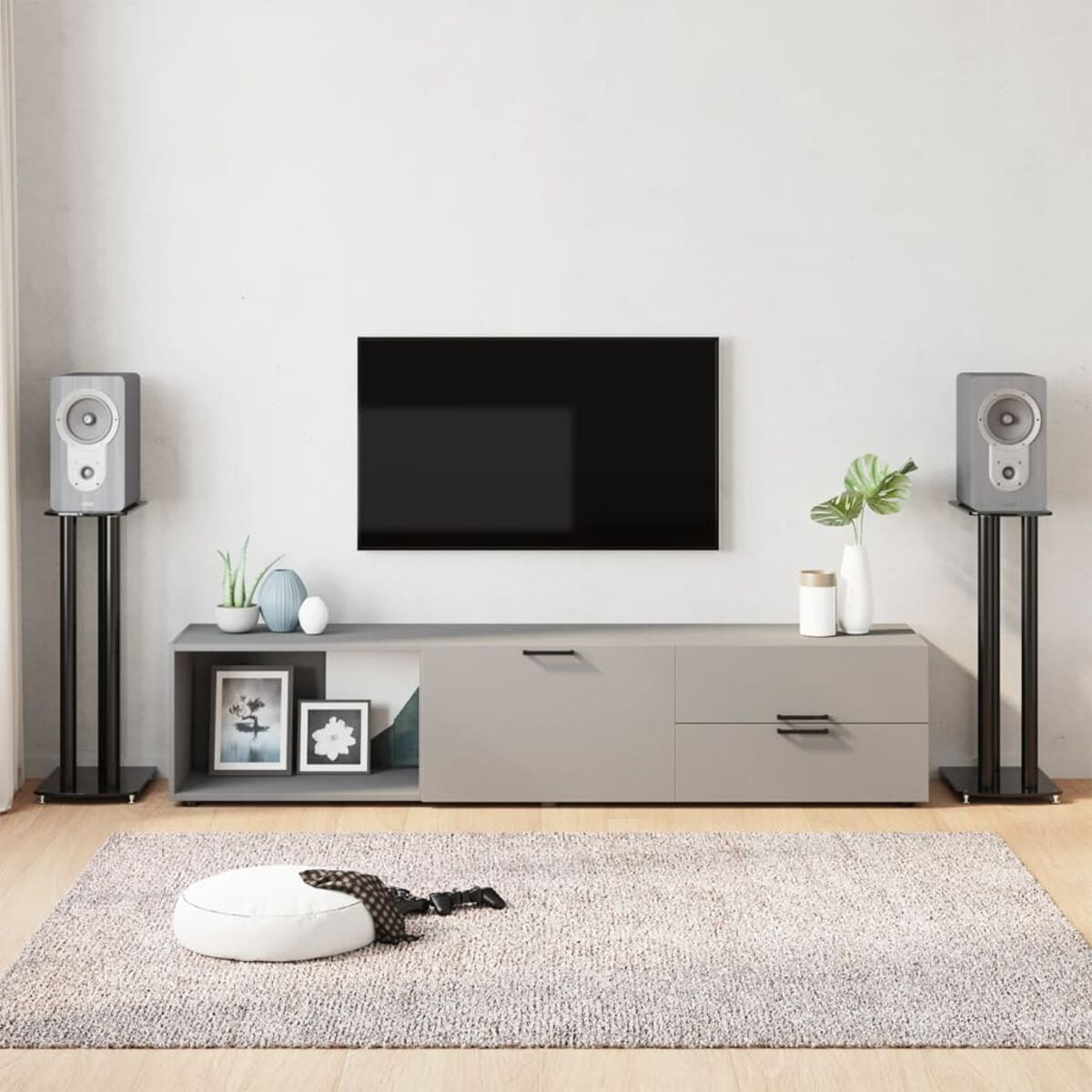 Wohnzimmer mit TV, Lautsprechern, grauem Schrank, weißem Teppich und dekorativen Gegenständen.