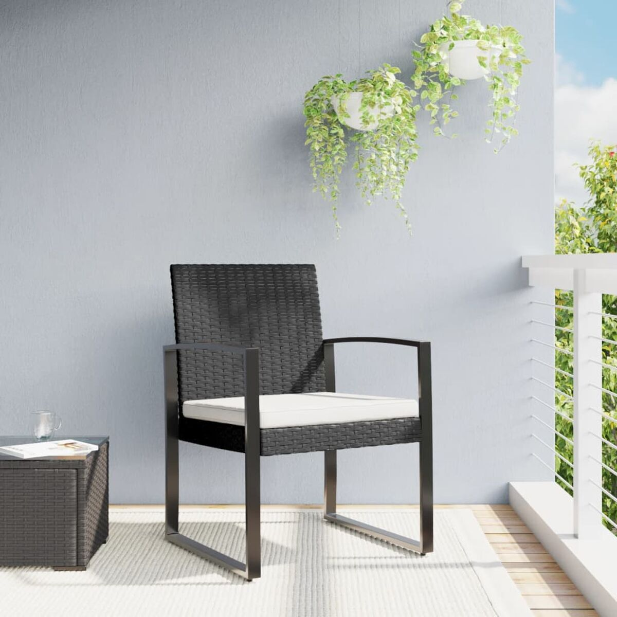 Schwarzer Outdoor-Stuhl aus Korbgeflecht mit Kissen, auf einer Terrasse mit Hängepflanzen und Tisch.