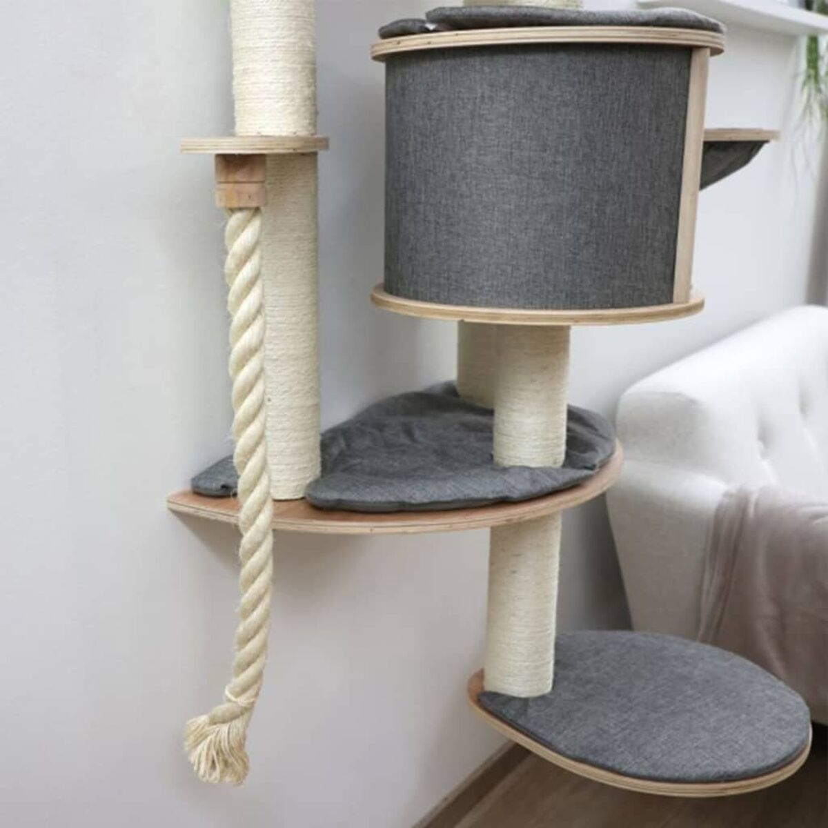 Katzenbaum mit mehreren Ebenen, einem Seil und grauen Kissen. Er steht vor einer weißen Wand.