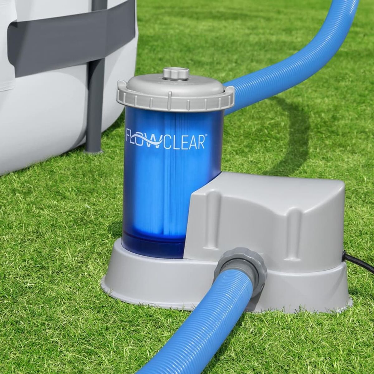 Ein blauer Poolfilter mit Schläuchen auf Gras. Das Wort FLOWCLEAR ist sichtbar.