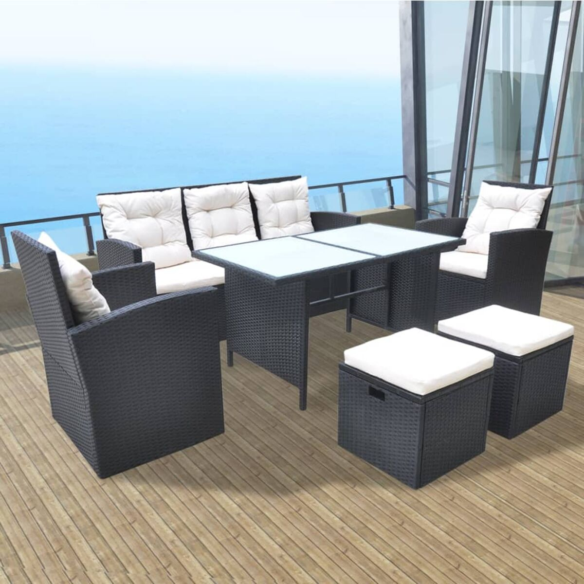 Schwarzes Outdoor-Essset aus Korbgeflecht. Beinhaltet Tisch, Sofa, Sessel und Ottomanen mit weißen Kissen. Meerblick.