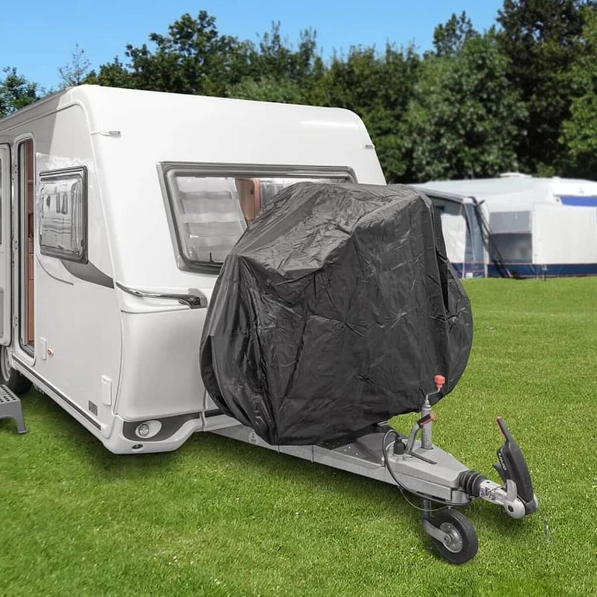 Ein weißer Wohnwagen mit schwarzer Abdeckung über der Anhängerkupplung. Auf Gras mit Bäumen und anderen Wohnwagen im Hintergrund.