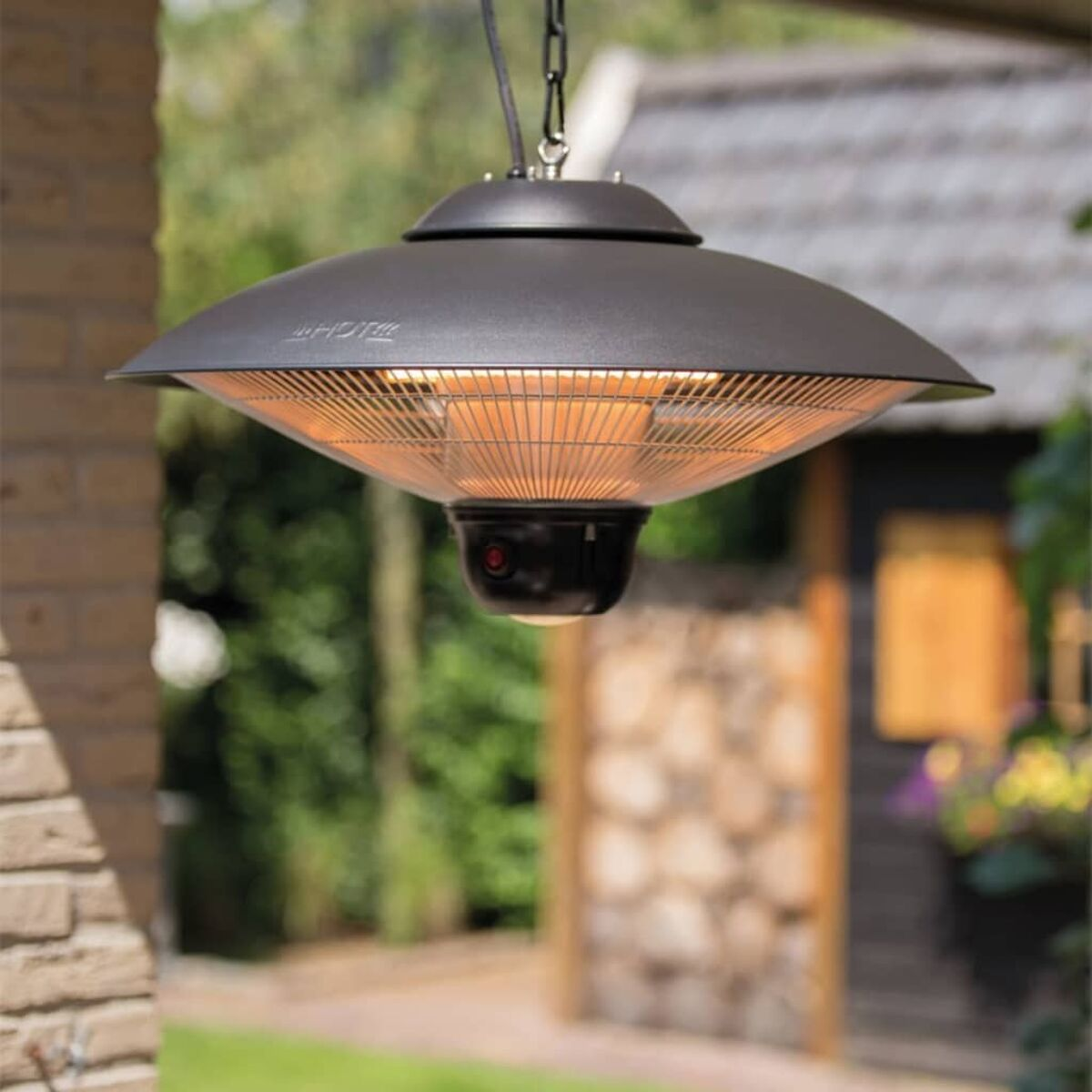 Black outdoor heater hanging with a red light, against a blurred green background.