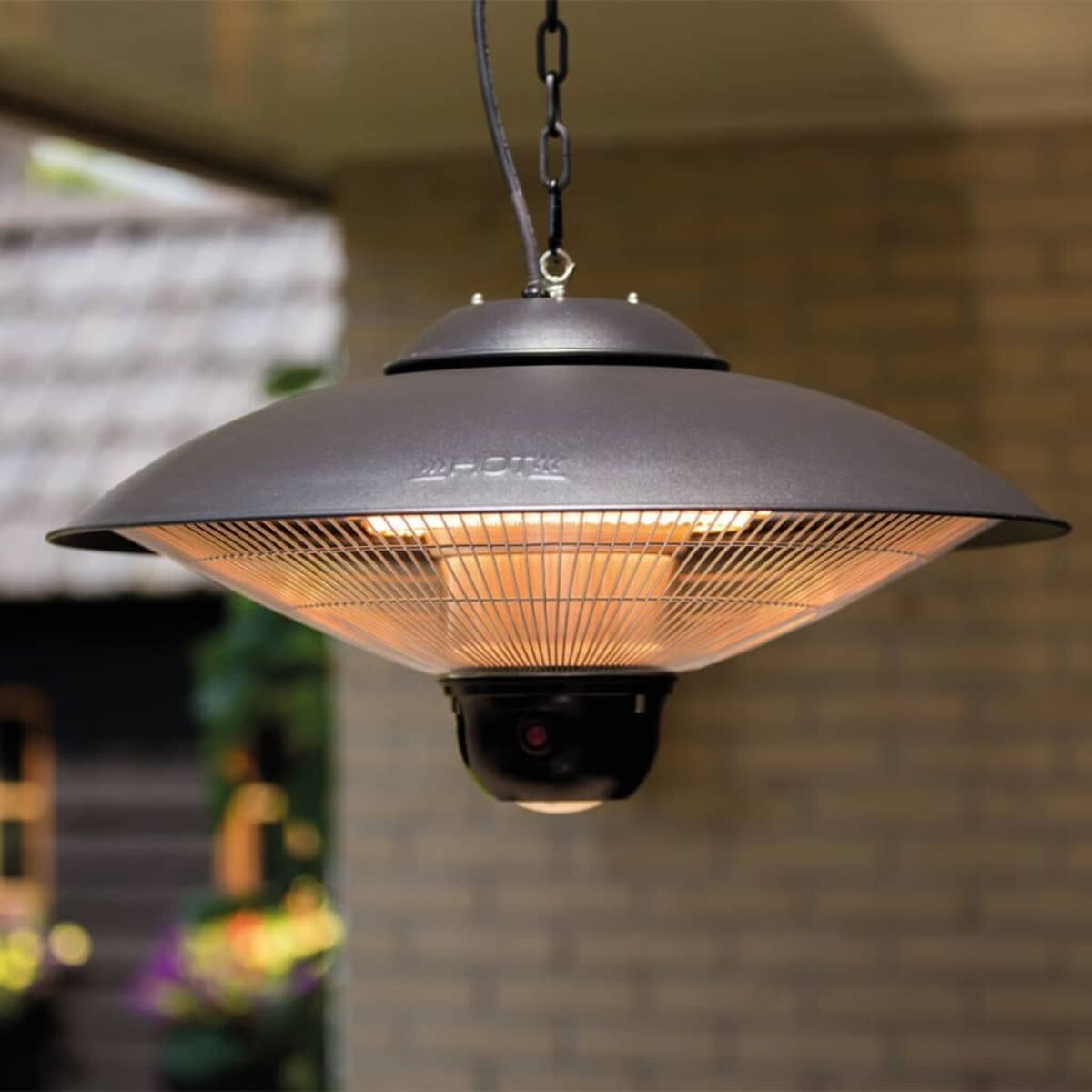 A black hanging outdoor heater with a heat element and a light. Placed against a brick wall.