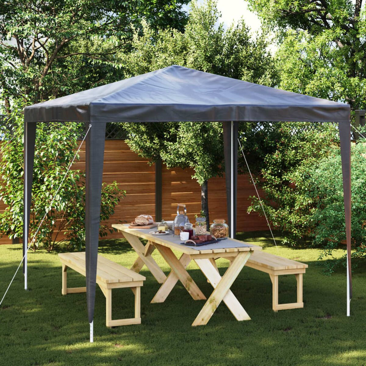 Ein Pavillon mit Tisch und Bänken, auf Gras. Bäume im Hintergrund.
