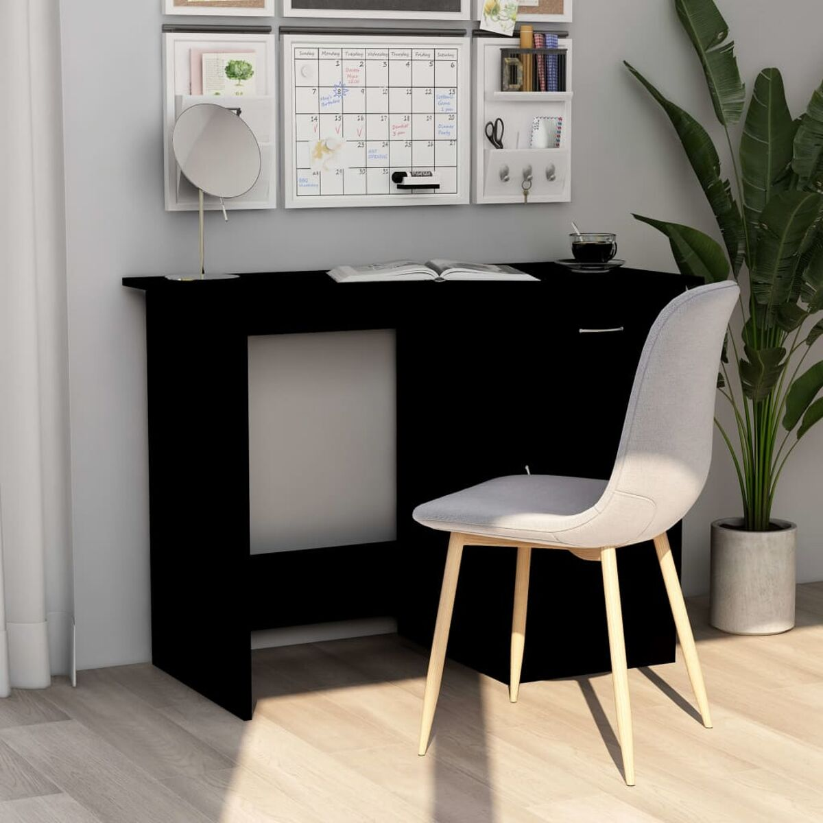 Ein schwarzer Schreibtisch mit Stuhl, an einer Wand mit Deko, Spiegel und Pflanze.
