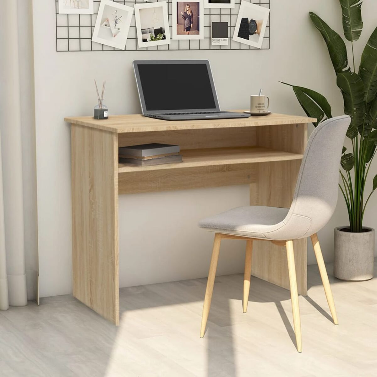 Ein Schreibtisch mit Laptop, Büchern und Tasse. Ein Drahtgitter mit Fotos im Hintergrund.